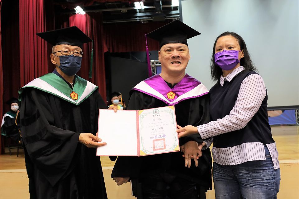 副校長吳聰能(左)代表頒發「校長特別獎」給腦麻博士生陳銘哲(中)。陳銘哲穿著「外骨骼機器人」人生第1次從輪椅站起來，由大姊陳秀玉(右)陪同領獎。