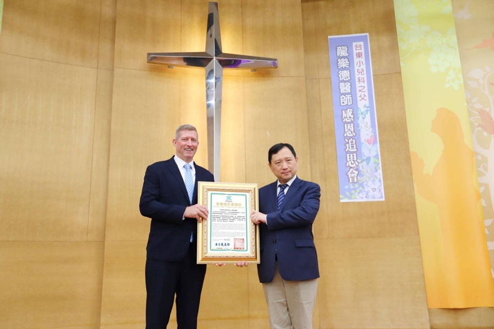 臺東縣副縣長王志輝(右)代表縣長頒發褒揚狀給榮譽縣民龍樂德醫師，由龍醫師次子Daniel代表接受。